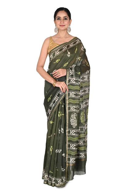 A model wearing an olive green Devyani hand block printed cotton-silk saree with white geometric and paisley patterns, paired with a gold sleeveless blouse by naitri.in
