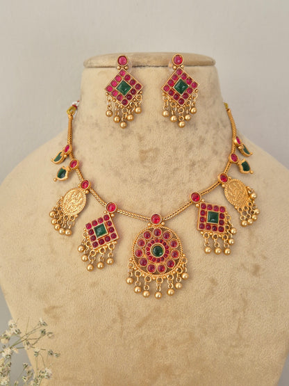 Gold-toned traditional Indian jewelry set featuring a necklace and matching earrings with red and green stone accents, for festive wear by naitri.in