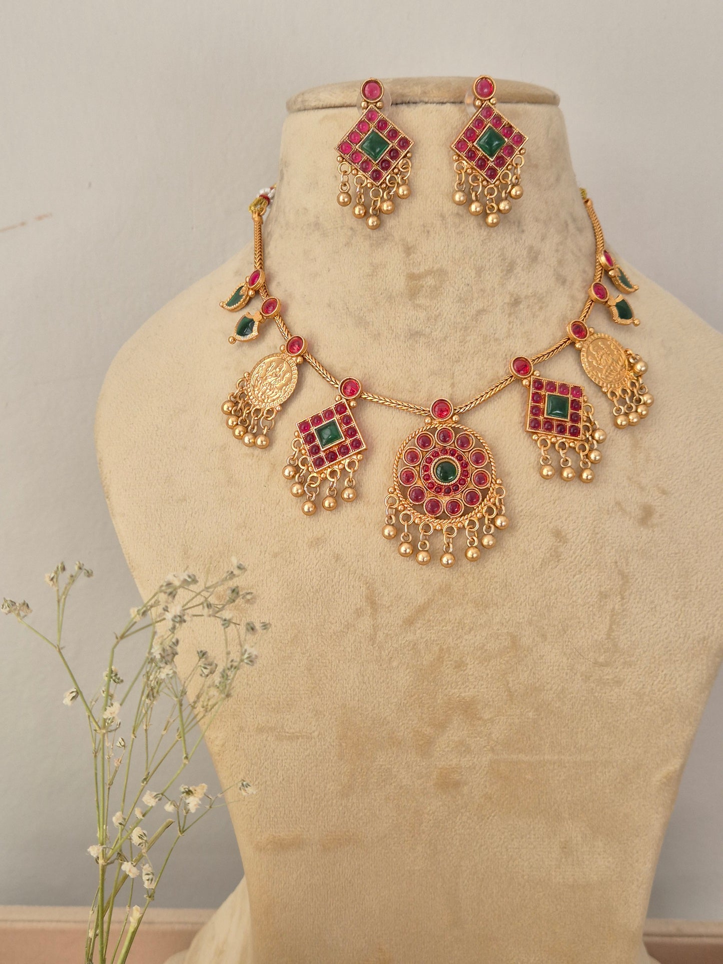 Gold-toned traditional Indian jewelry set featuring a necklace, earrings decorated with red and green stones by naitri.in