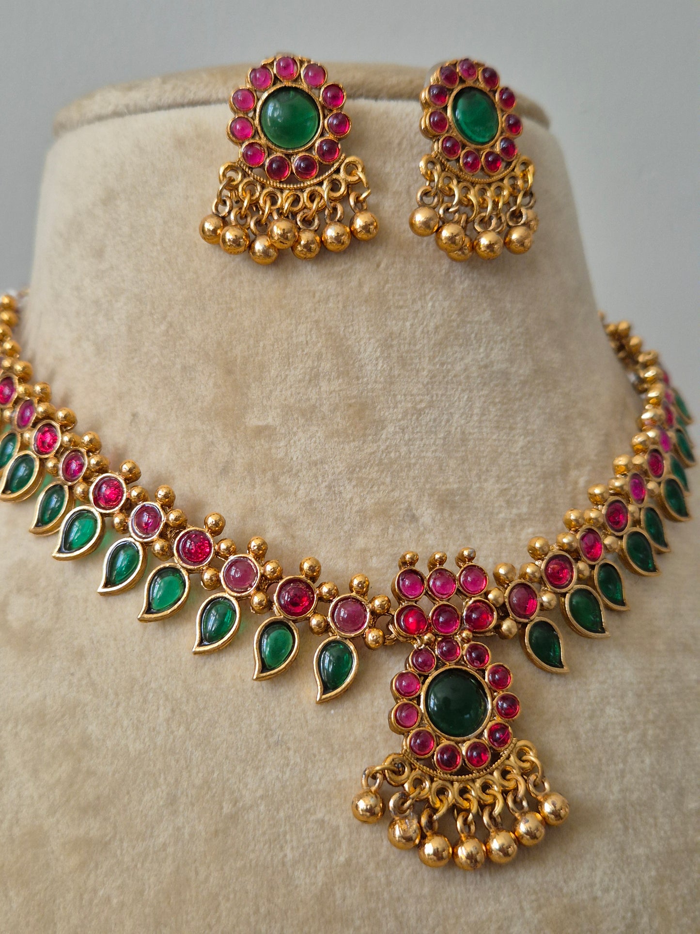  Gold-finish brass alloy necklace with ruby-red and emerald-green stones and matching earrings by naitri.in