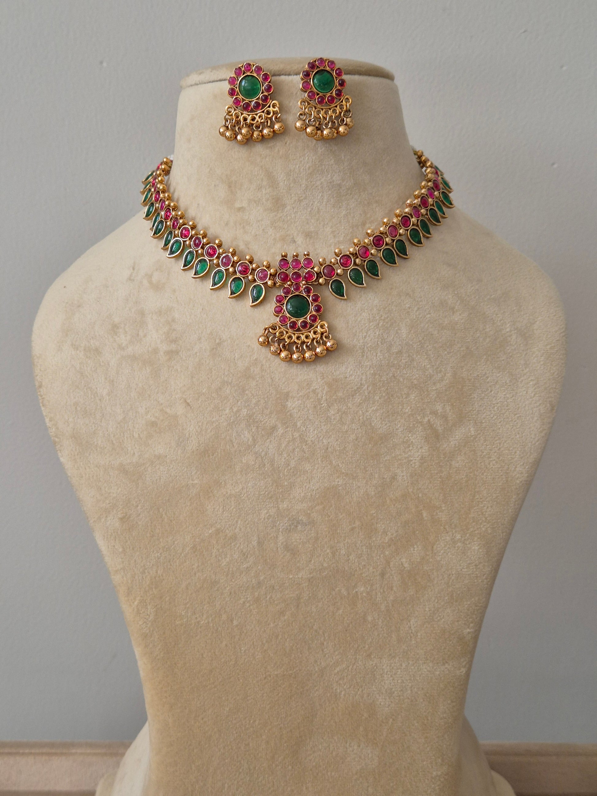 Gold-plated choker necklace featuring intricate red and green stonework with matching stud earrings by naitri.in