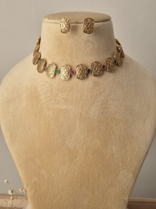 Diksha Necklace Set featuring a golden brass choker with geometric motifs, red and green gemstone accents, and matching stud earrings by naitri.in