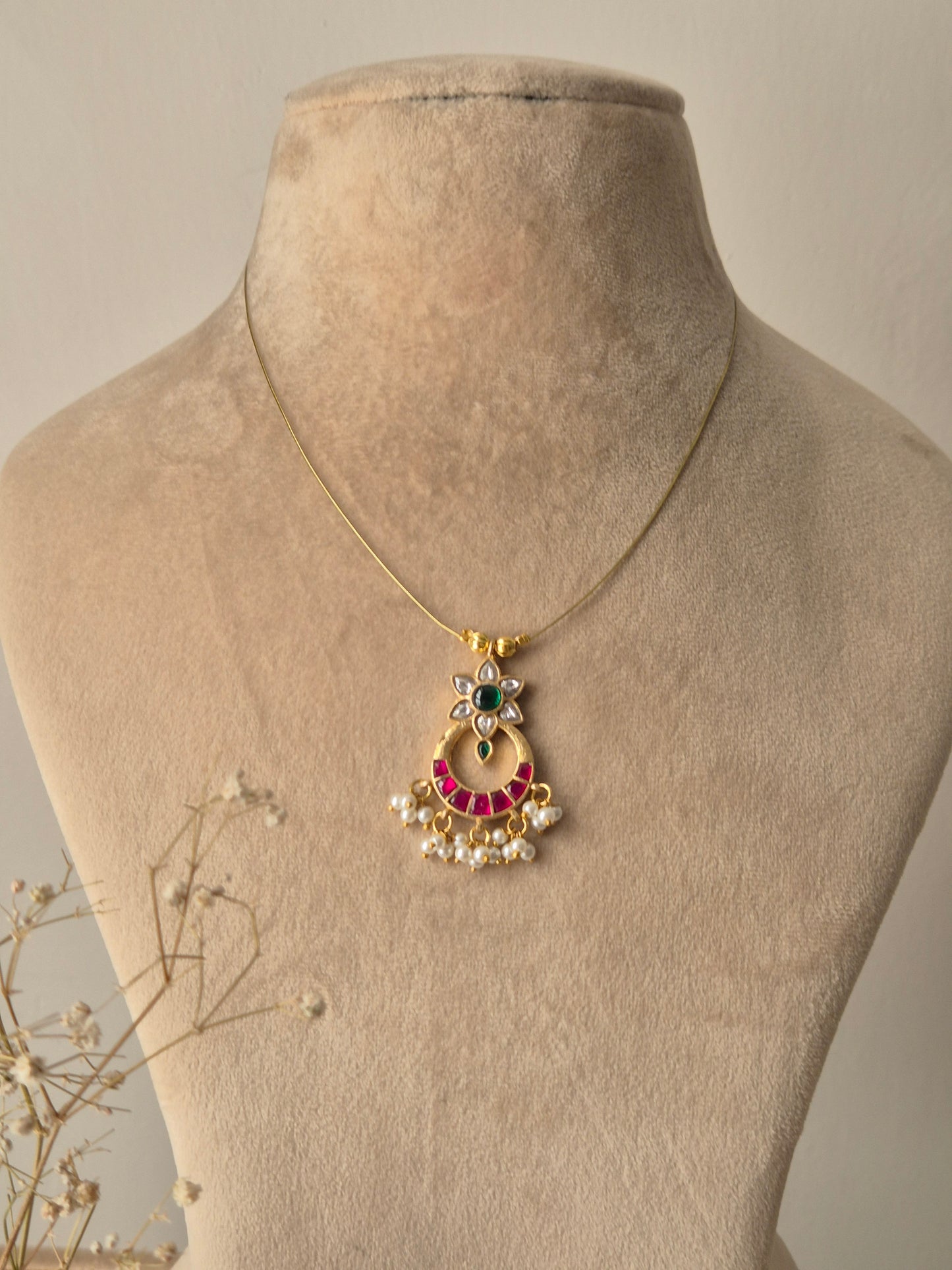 Handcrafted necklace featuring a gold-toned crescent moon pendant adorned with pink stones, a central green emerald-like stone, and delicate white pearl droplets on a minimalist thin chain by naitri.in