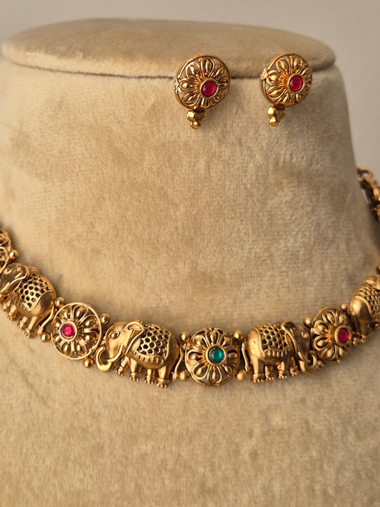 Disha Necklace Set featuring a handcrafted golden choker with elephant motifs, red and green gemstone accents, and matching stud earrings by naitri.in
