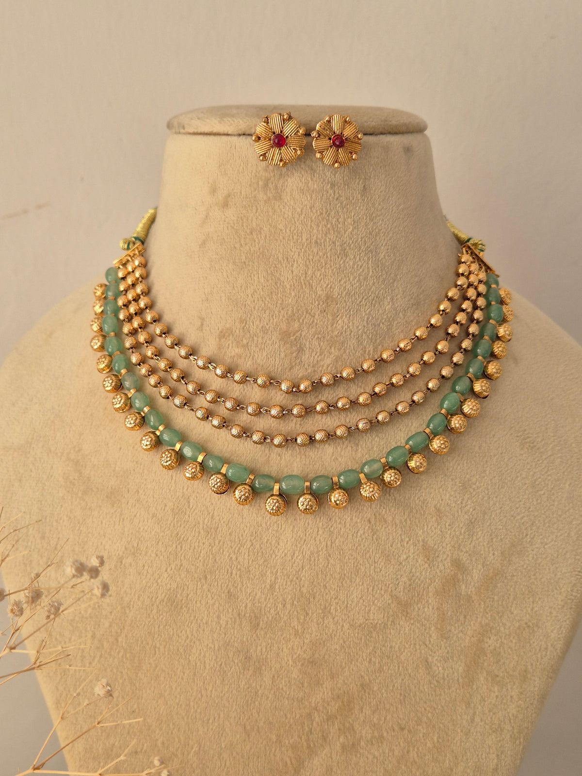 Ornate Multi-Row Bead Necklace and Studs presented on a display bust, emphasizing the sophisticated layered design, contrasting green and gold tones, and classic styling by Naitri.in