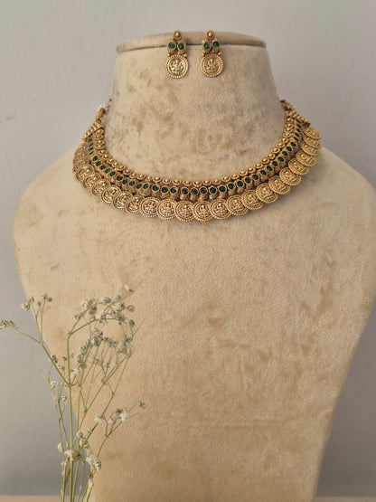 Gold-toned traditional Indian jewelry set The choker necklace features a row of circular coin-style motifs detailed with intricate borders and dark green gemstone accents, paired with matching small hanging coin earrings, by naitri.in