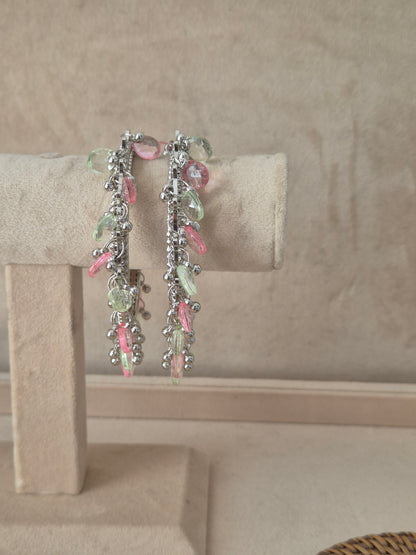 Set of two oxidized silver Eartha bangles hanging from a beige velvet display stand, featuring a row of dangling, faceted pastel pink and mint green teardrop gemstones and small metallic beads by naitri.in
