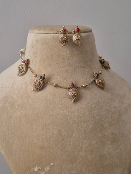 Handcrafted gold necklace and earring set with red and green gemstone embellishments on a minimalist chain by naitri.in
