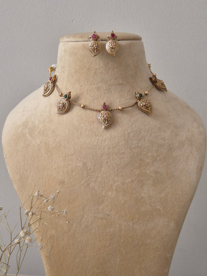 Set by Naitri featuring a gold-plated brass chain with five leaf-shaped pendants, red and green stone accents, and matching leaf-shaped stud earrings