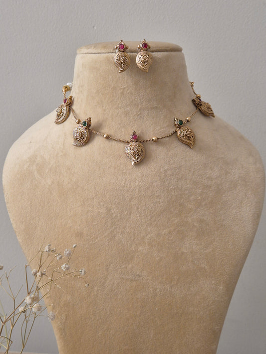 Set by Naitri featuring a gold-plated brass chain with five leaf-shaped pendants, red and green stone accents, and matching leaf-shaped stud earrings