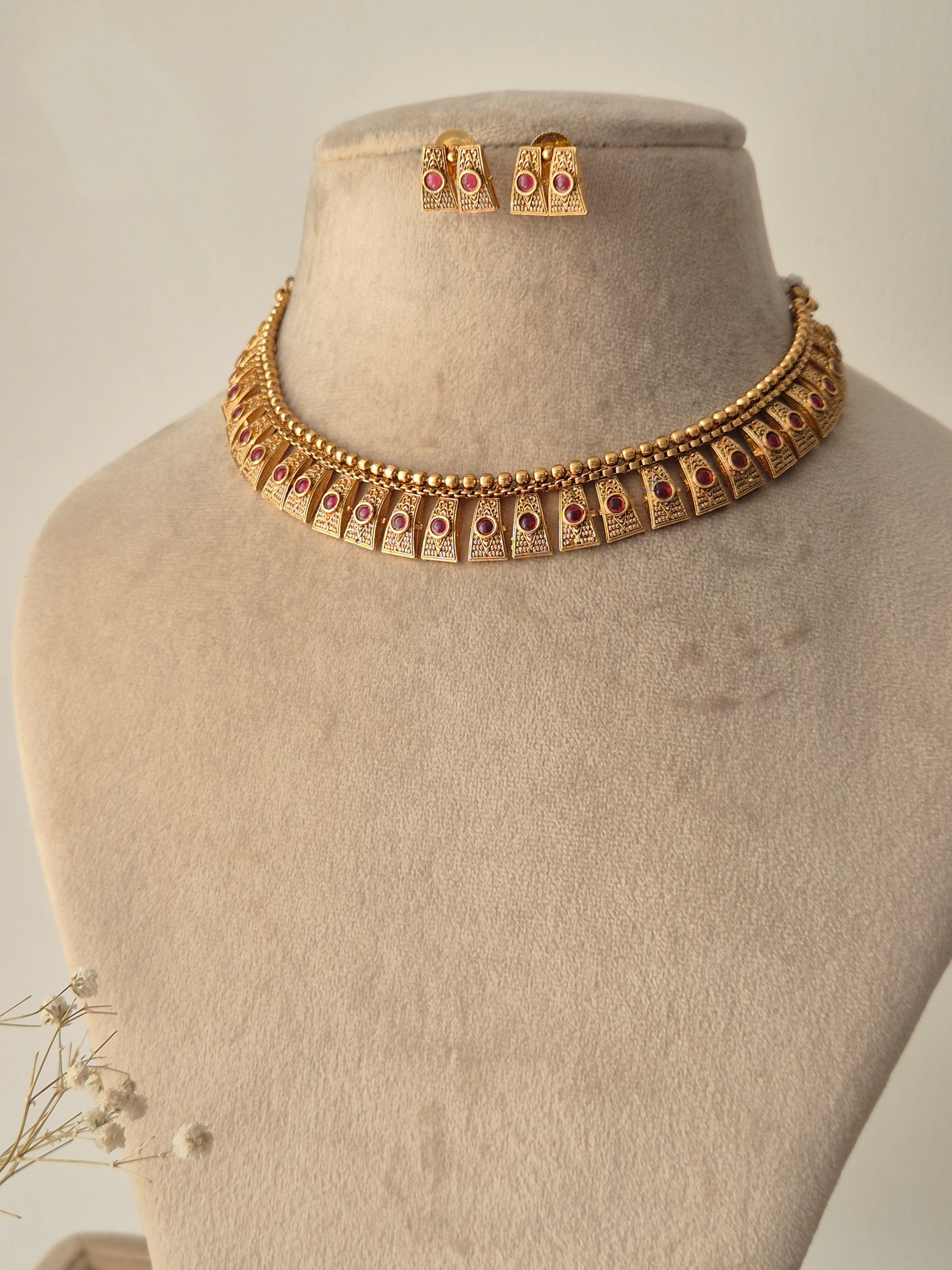 Hammered gold finish necklace set, Close-up of the filigree metalwork and red stone settings on a gold-plated brass choker by naitri.in