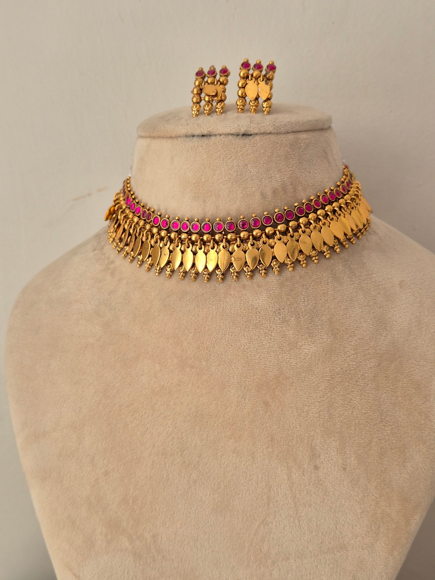 Gold-toned traditional necklace set  featuring a choker with gold leaf-like drops and a row of pink stones, plus matching earrings by naitri.in