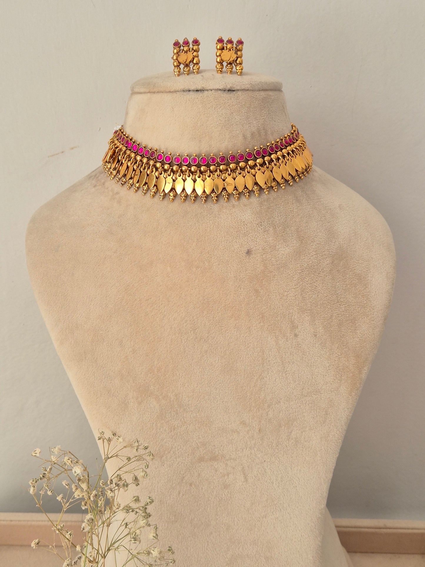 A gold-toned traditional choker necklace with a row of pink stones, Matching gold earrings with pink stones by naitri.in