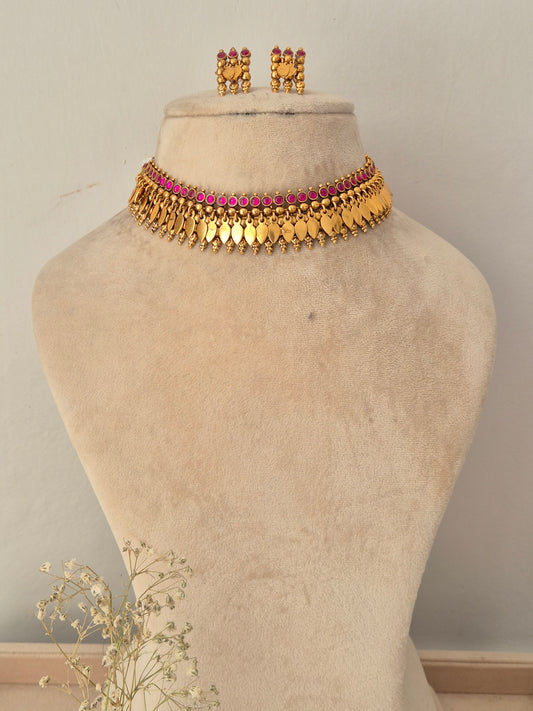 A gold-toned traditional choker necklace with a row of pink stones, Matching gold earrings with pink stones by naitri.in