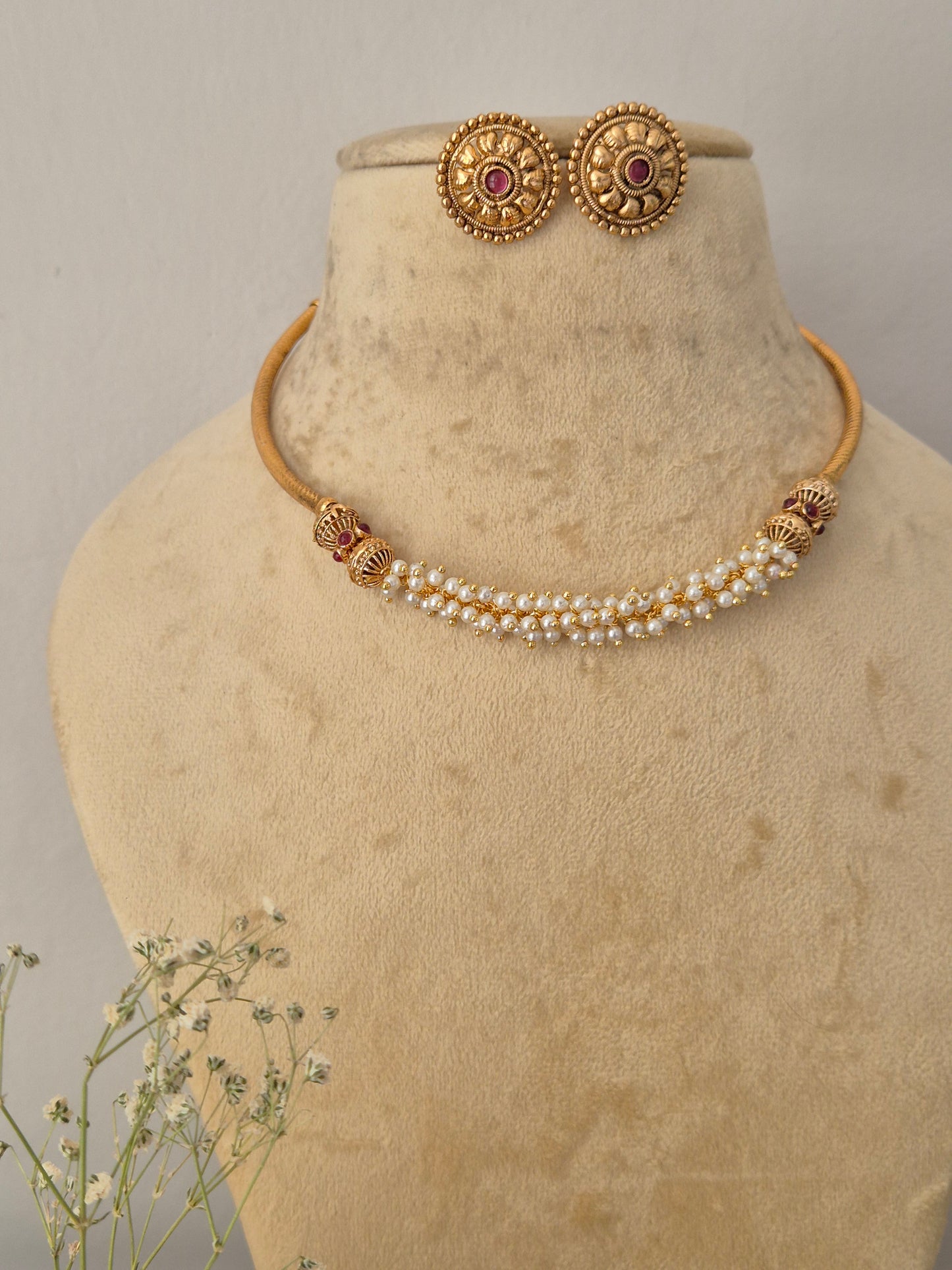 Gold-toned traditional Indian jewelry set, featuring a pearl-beaded choker with gold-toned decorative elements and matching round stud earrings with red stone centers by naitri.in 