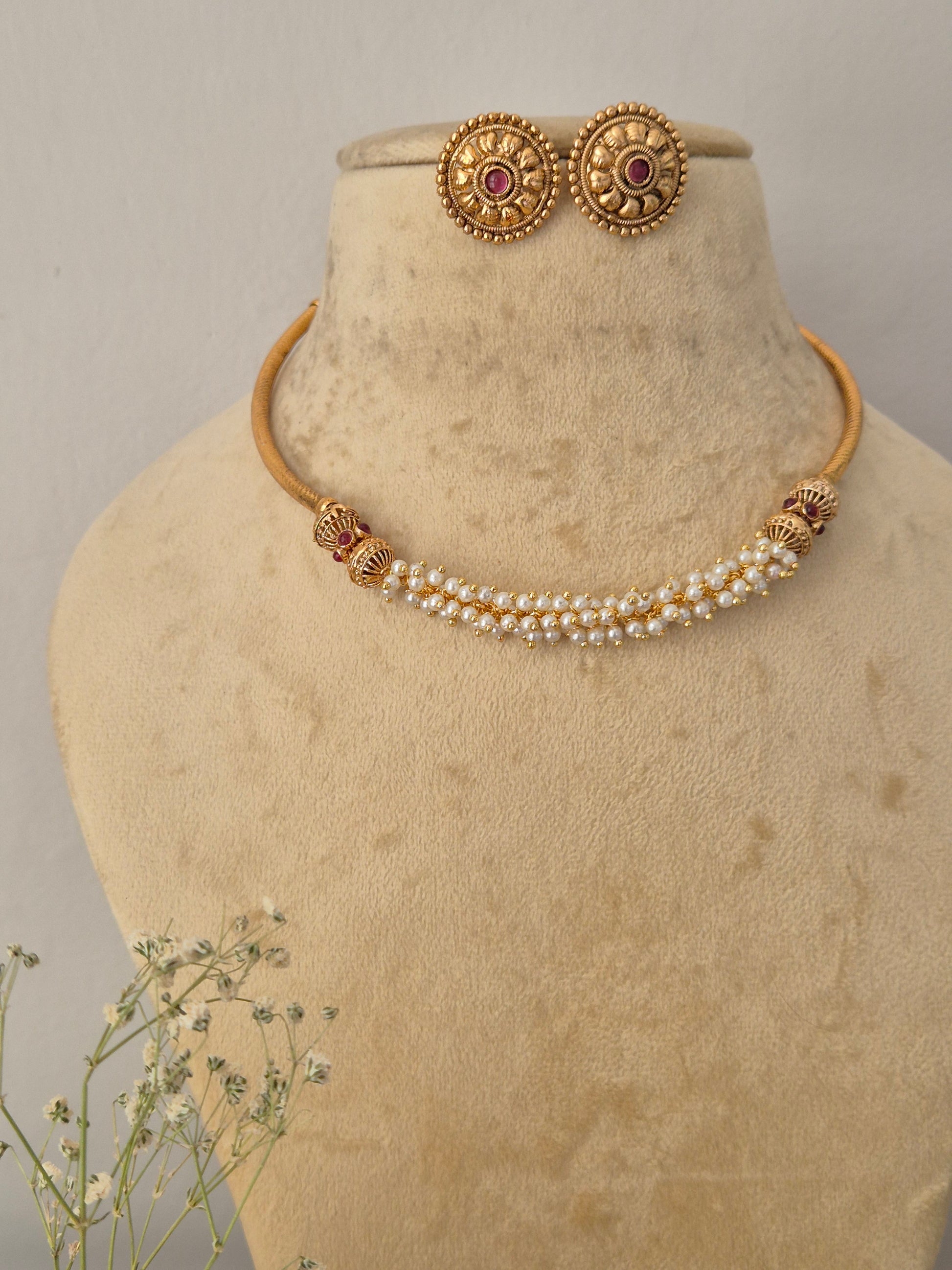 Gold-toned traditional Indian jewelry set, featuring a pearl-beaded choker with gold-toned decorative elements and matching round stud earrings with red stone centers by naitri.in 