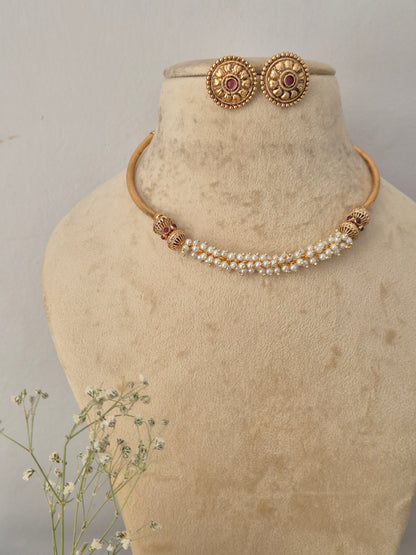 Gold-toned traditional jewelry set, including a pearl-beaded necklace with gold-toned spacer details and matching round stud earrings with red gemstone center by naitri.in