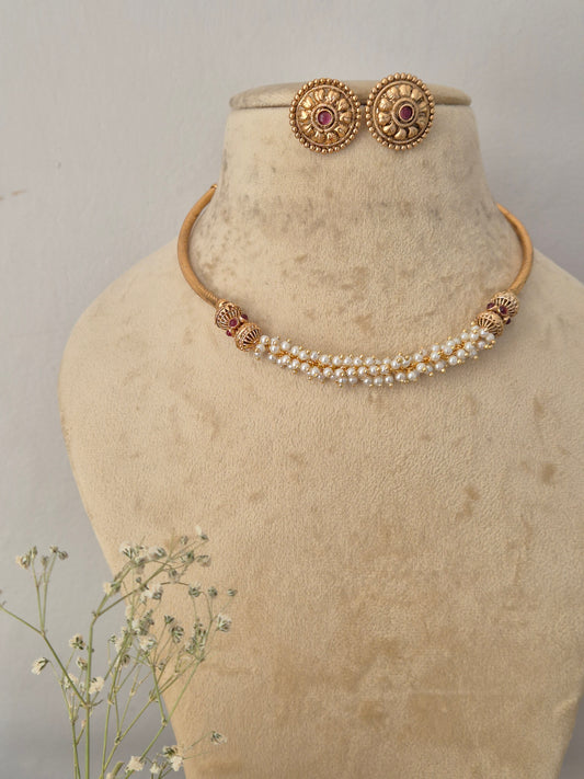 Gold-toned traditional jewelry set, including a pearl-beaded necklace with gold-toned spacer details and matching round stud earrings with red gemstone center by naitri.in