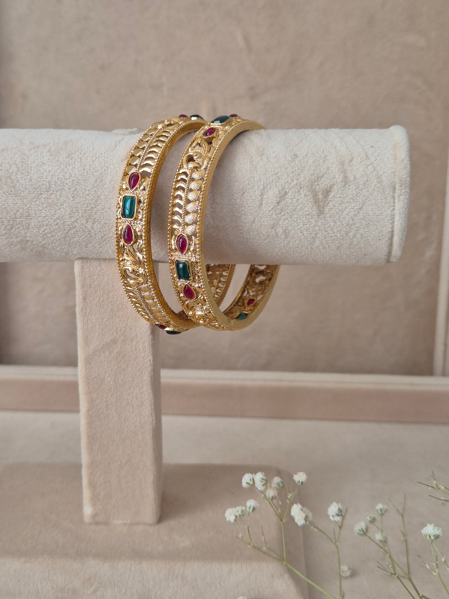 Pair of Naitri's Esha gold bangles showcasing detailed ethnic craftsmanship, embedded with vibrant pinkish-red and green accent stones by naitri.in