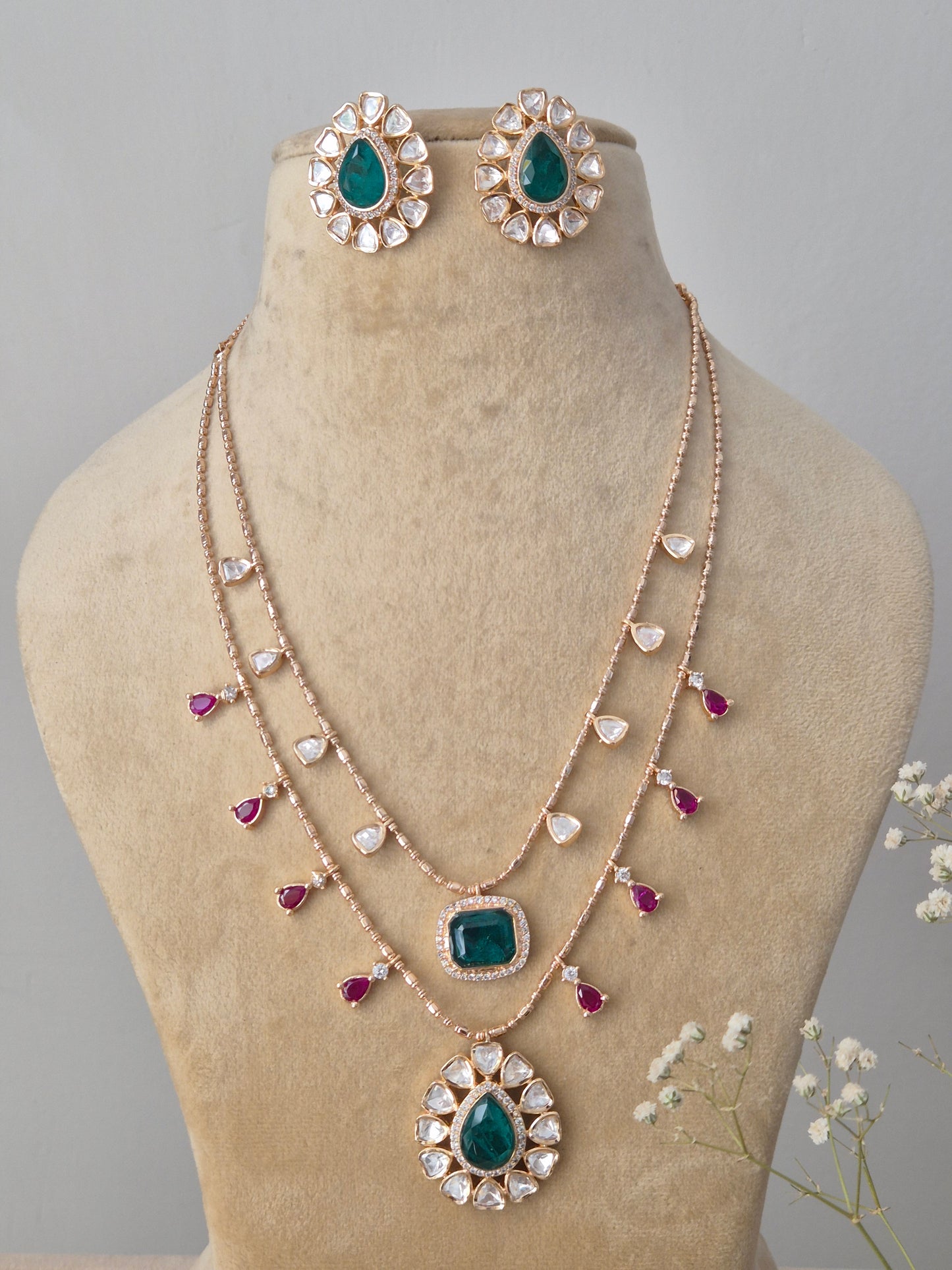A double-layered rose-gold plated chain featuring emerald-green square pendants, ruby-pink teardrop accents pendant, and matching green stone stud earring by naitri.in