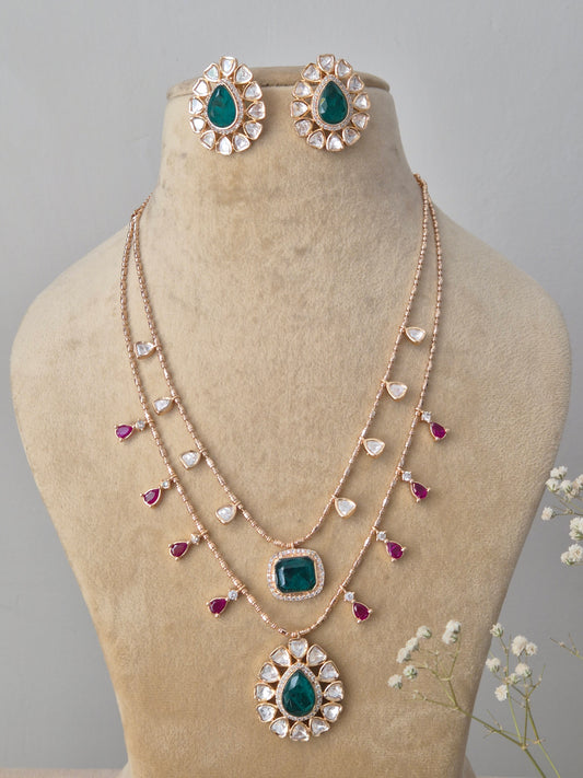 A double-layered rose-gold plated chain featuring emerald-green square pendants, ruby-pink teardrop accents pendant, and matching green stone stud earring by naitri.in