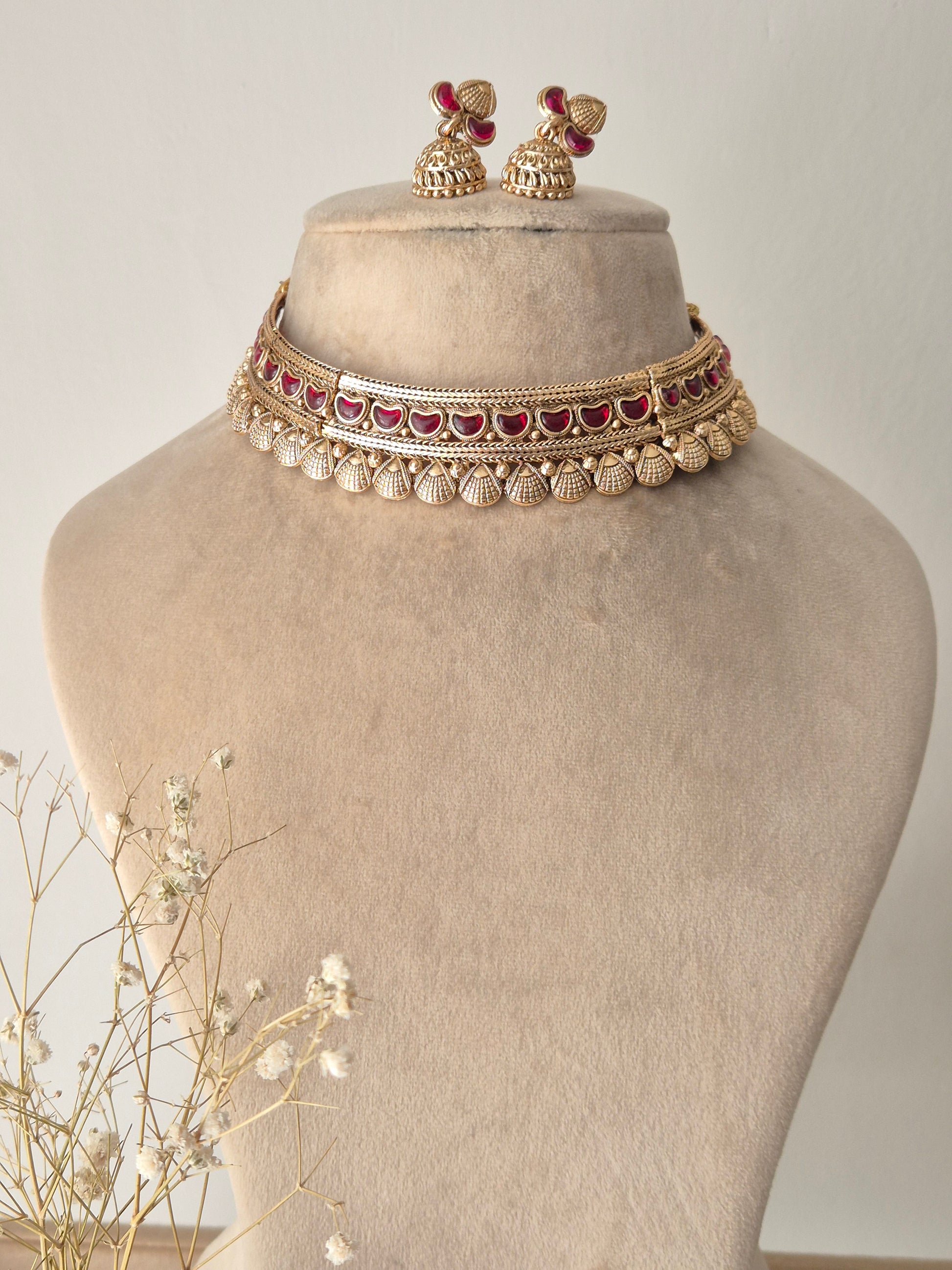 Handcrafted gold-plated brass choker necklace with intricate red stone embellishments and matching jhumka earrings by naitri.in
