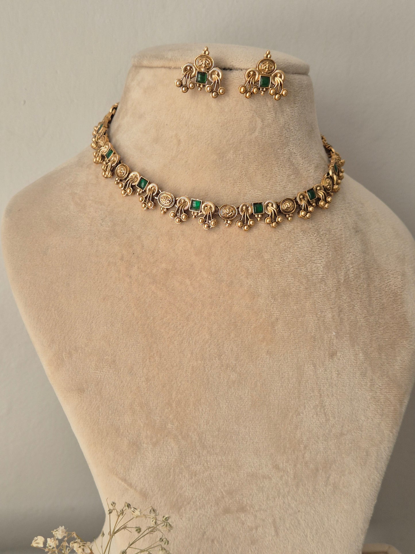 Gold-toned traditional jewelry set including a choker necklace and matching earrings with green stone accents by naitri.in