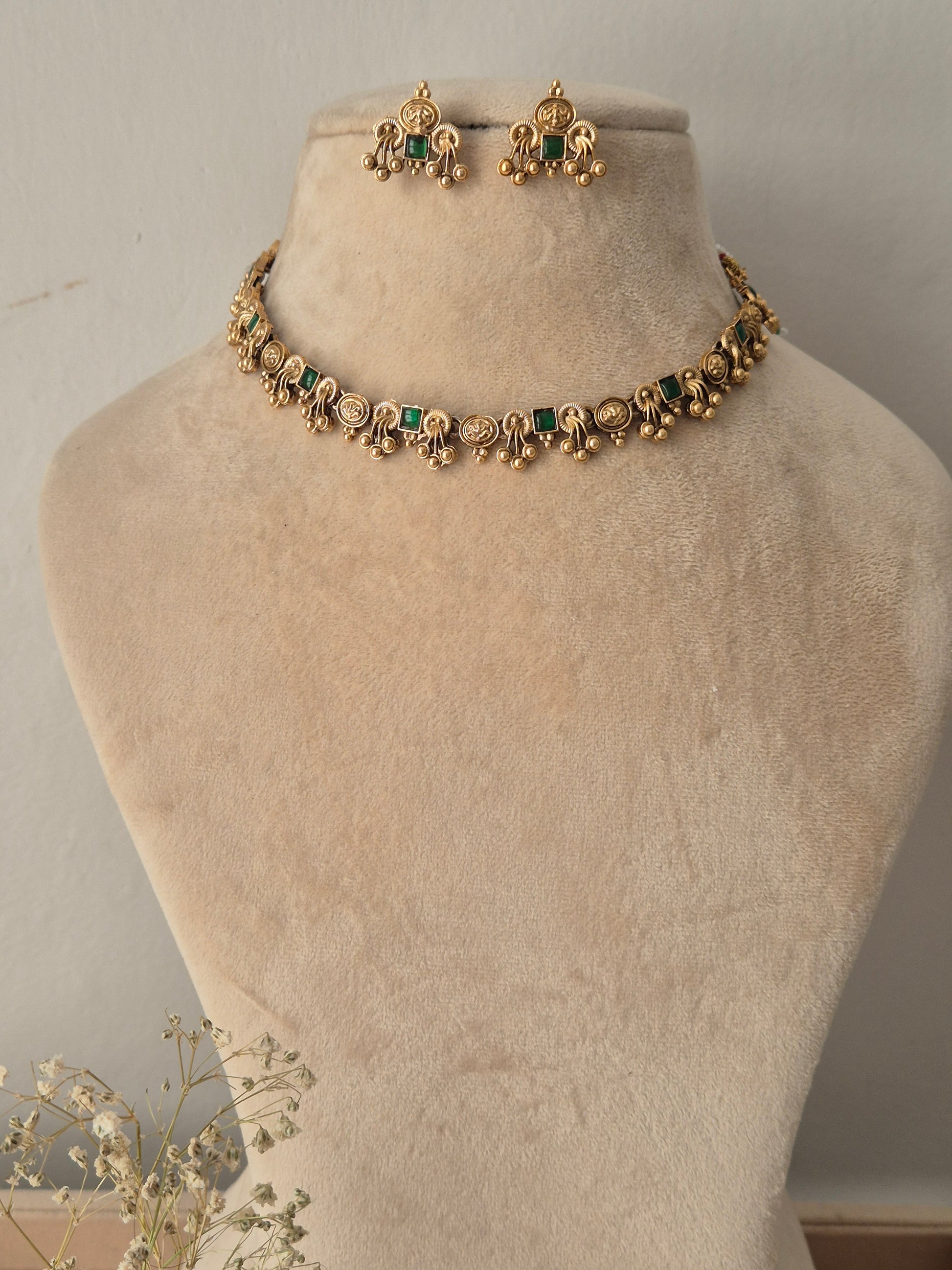 Gold-toned traditional jewelry set , including a necklace and matching earrings with green stone accents by naitri.in