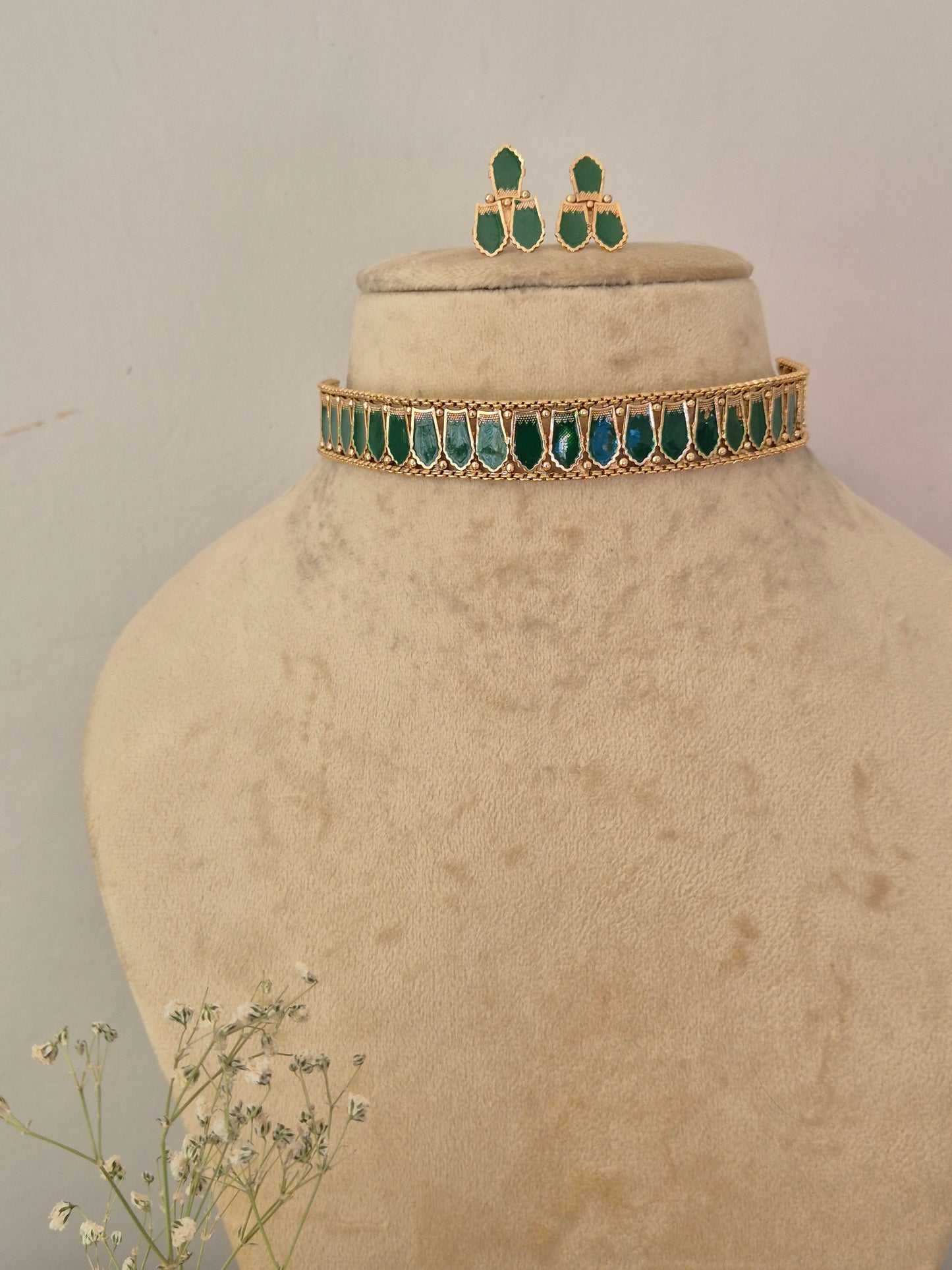Gold-toned jewelry set, featuring a choker-style necklace with green teardrop-shaped stones and matching drop earrings by naitri.in