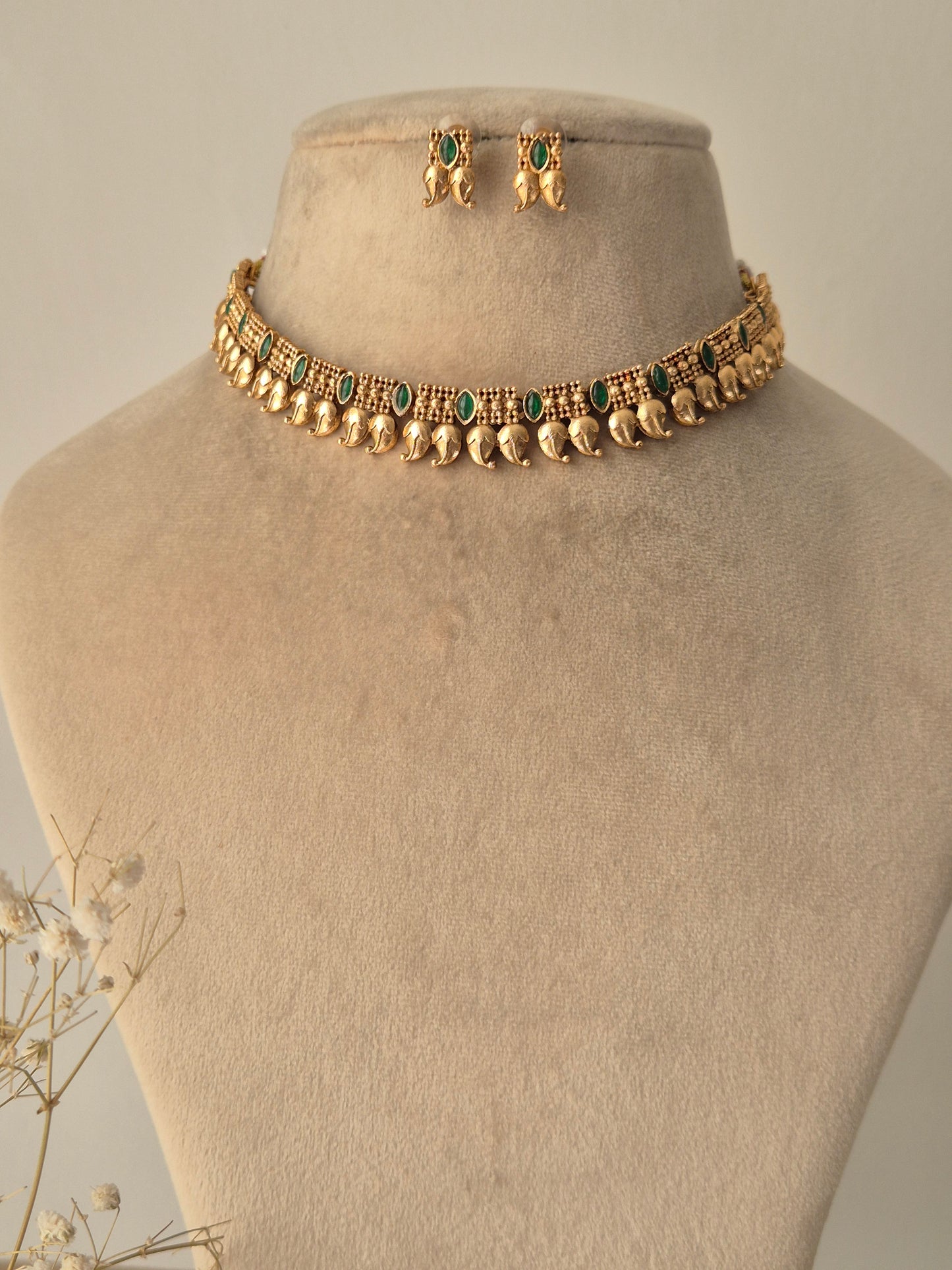 Gold necklace with leaf drop design attached fir gold plated chain and green stones attached in chain same designed earrings by naitri.in