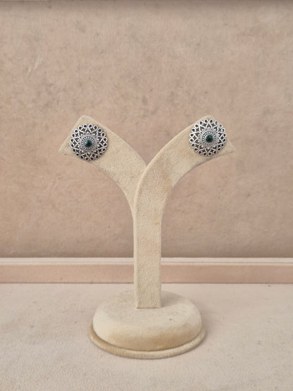 A pair of silver-toned filigree stud earrings with dark blue-green stone centers, by naitri.in