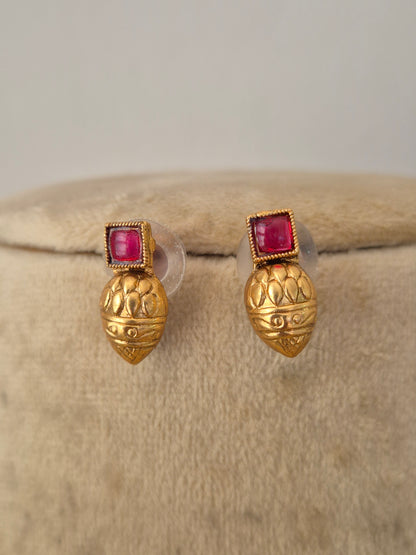 A pair of gold post earrings with a textured, lotus-like gold top and a square pinkish-red gemstone in a beaded border setting, by naitri.in