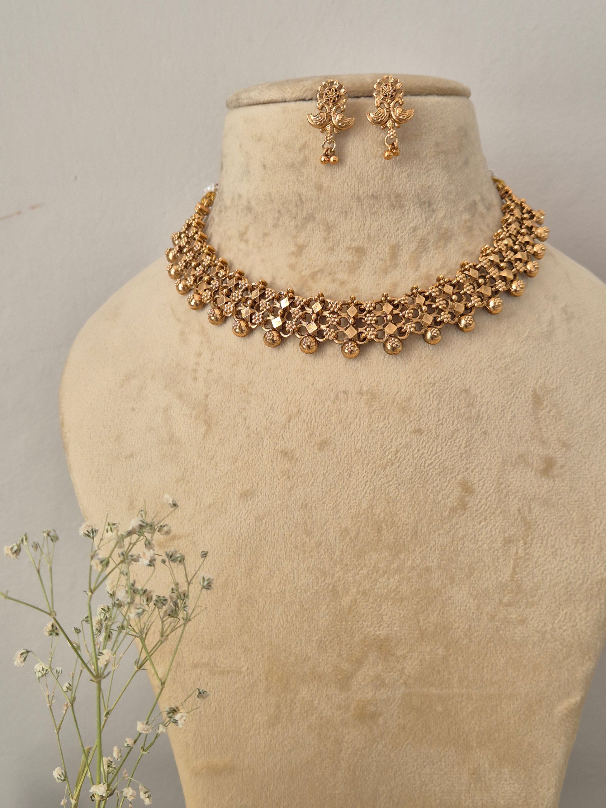 Gold-plated Indian choker necklace and matching dangle earrings set the necklace features an intricate, textured mesh-like weave pattern accented by hanging small gold beads, with matching floral-motif drop earrings by naitri.in
