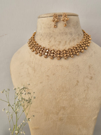 Gold-plated Indian choker necklace and matching dangle earrings set the necklace features an intricate, textured mesh-like weave pattern accented by hanging small gold beads, with matching floral-motif drop earrings by naitri.in