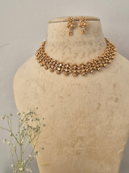 Gold-plated Indian choker necklace and matching dangle earrings set the necklace features an intricate, textured mesh-like weave pattern accented by hanging small gold beads, with matching floral-motif drop earrings by naitri.in