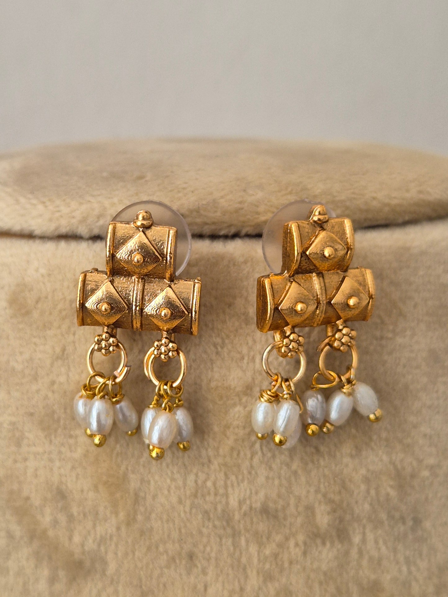 A pair of gold-toned traditional earrings with textured geometric cube charms, small gold bead details, and dangling white pearl-like drops, by naitri.in