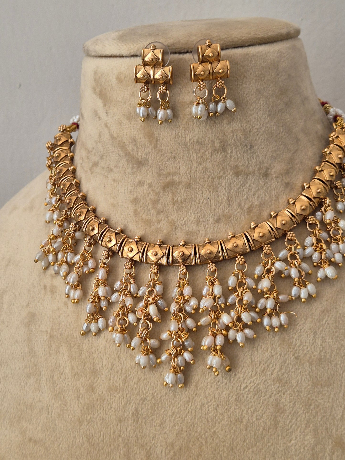 Gold-toned traditional Indian jewelry set featuring a statement necklace and matching earrings with white pearl-like beads, by naitri.in