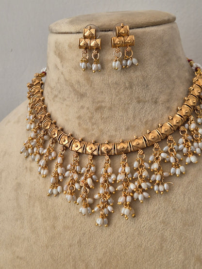 Gold-toned traditional Indian jewelry set featuring a statement necklace and matching earrings with white pearl-like beads, by naitri.in
