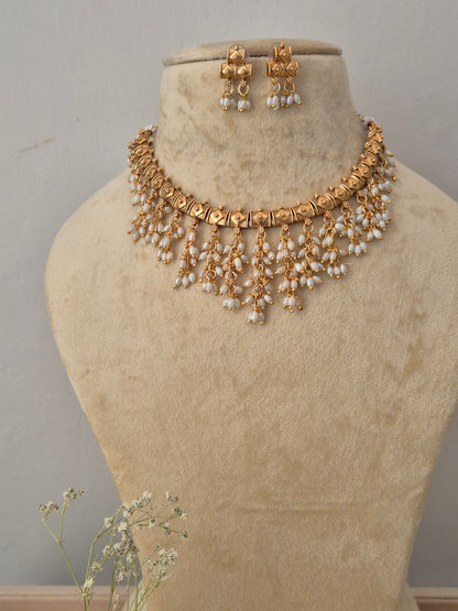 Gold-toned traditional choker necklace and matching dangle earrings features a patterned metallic collar adorned with cascading, multi-layered rows of pointed white pearl droplets, paired with matching small hanging earrings also finished with pearl drops by naitri.in