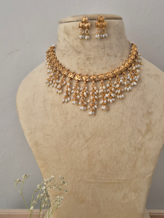 Gold-toned traditional choker necklace and matching dangle earrings features a patterned metallic collar adorned with cascading, multi-layered rows of pointed white pearl droplets, paired with matching small hanging earrings also finished with pearl drops by naitri.in