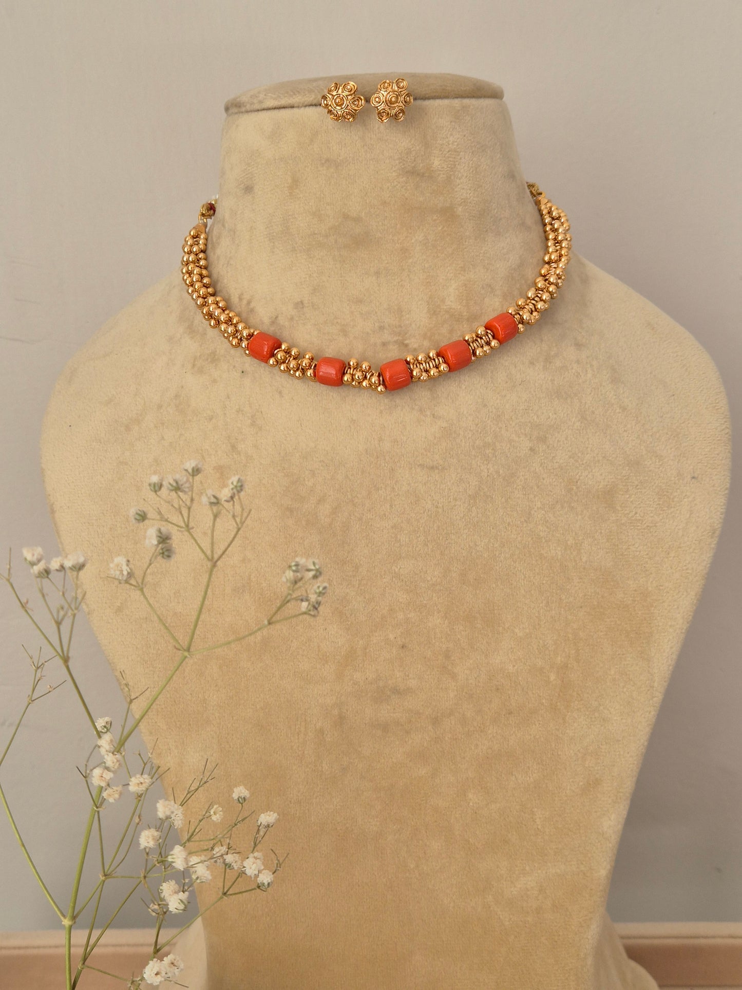 Handcrafted gold-plated collar choker necklace featuring a row of smooth coral-red beads and textured gold spacer beads, with matching round gold stud earrings by naitri.in