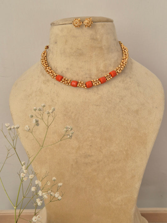 Handcrafted gold-plated collar choker necklace featuring a row of smooth coral-red beads and textured gold spacer beads, with matching round gold stud earrings by naitri.in
