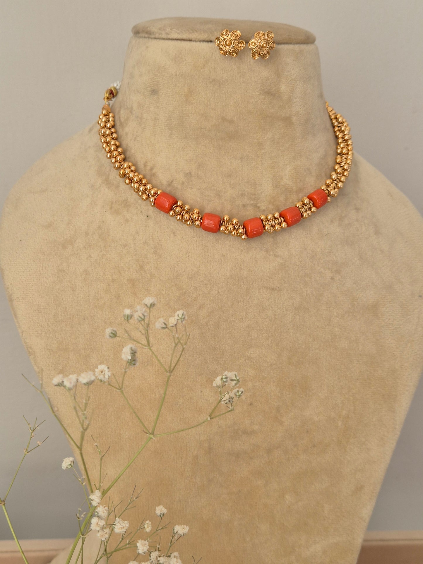 Artisanal Fiza necklace and earring set in a modern ethnic aesthetic,Gold-polished minimalist choker with coral-red stone embellishments and coordinating textured stud earrings. by naitri.in