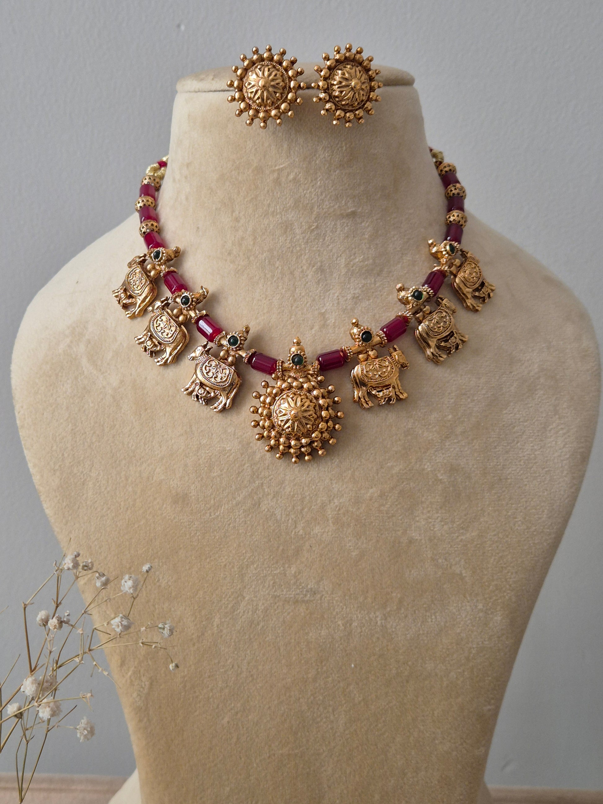 Set featuring gold-toned temple jewelry with bird motifs, red beads, and matching circular stud earrings by naitri.in