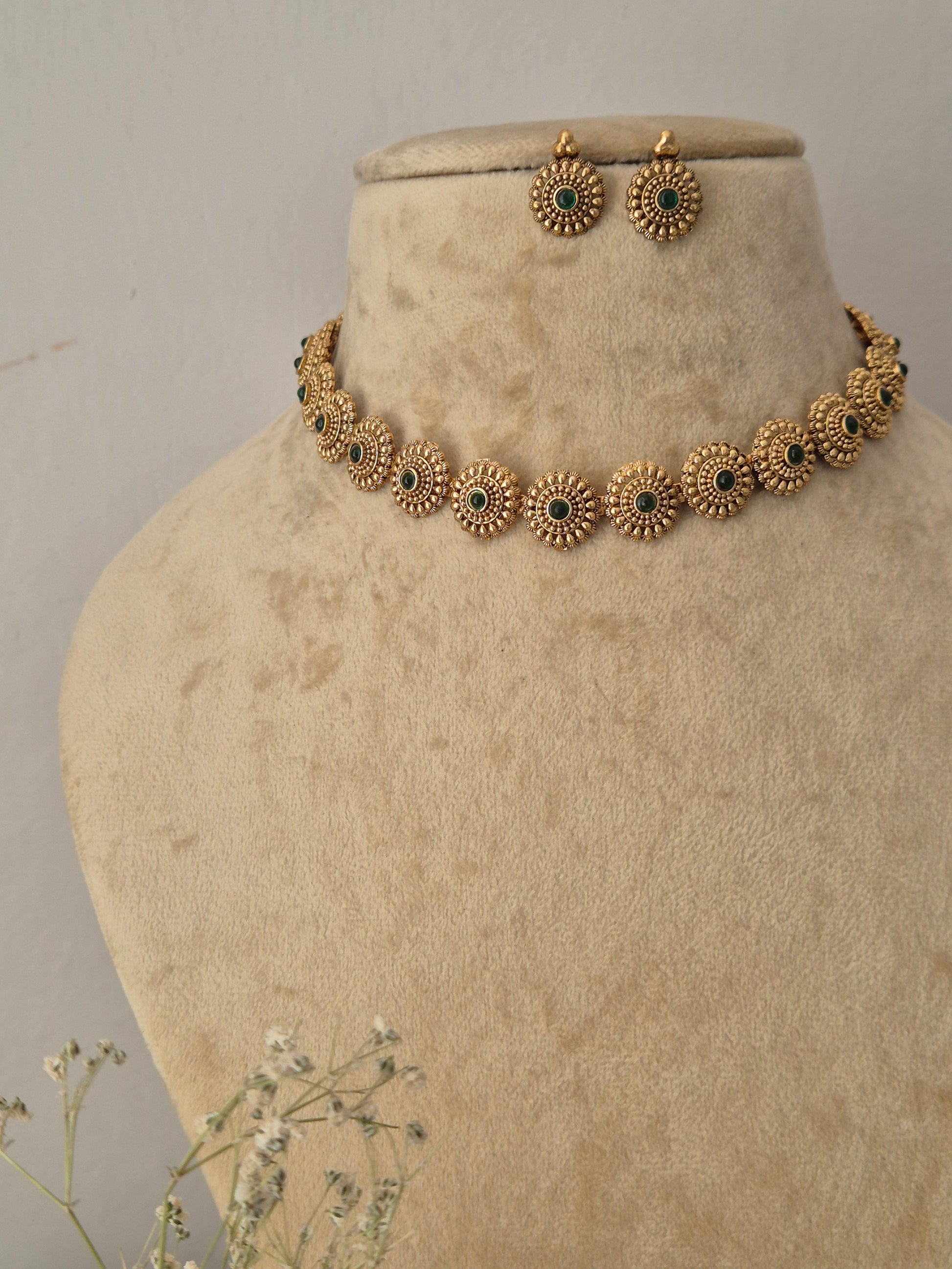 Antique gold-toned choker necklace set with green gemstones and circular textured motifs. Naitri featuring an antique gold-plated ethnic choker and matching traditional stud earrings with green stones by naitri.in