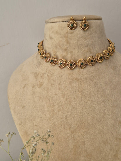 Antique gold-toned choker necklace set with green gemstones and circular textured motifs. Naitri featuring an antique gold-plated ethnic choker and matching traditional stud earrings with green stones by naitri.in