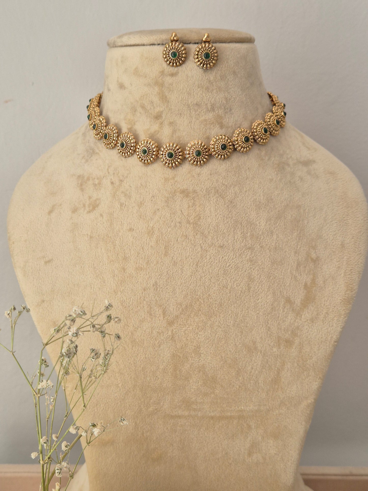 Gold-toned jewelry set featuring a floral-patterned necklace and matching earrings with small green stone accents, by naitri.in