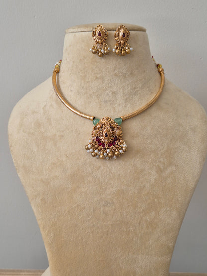 gold-plated necklace set featuring a temple-style pendant with ruby pink stones, green bead accents, and white pearl droplets with matching jhumka earrings by naitri.in