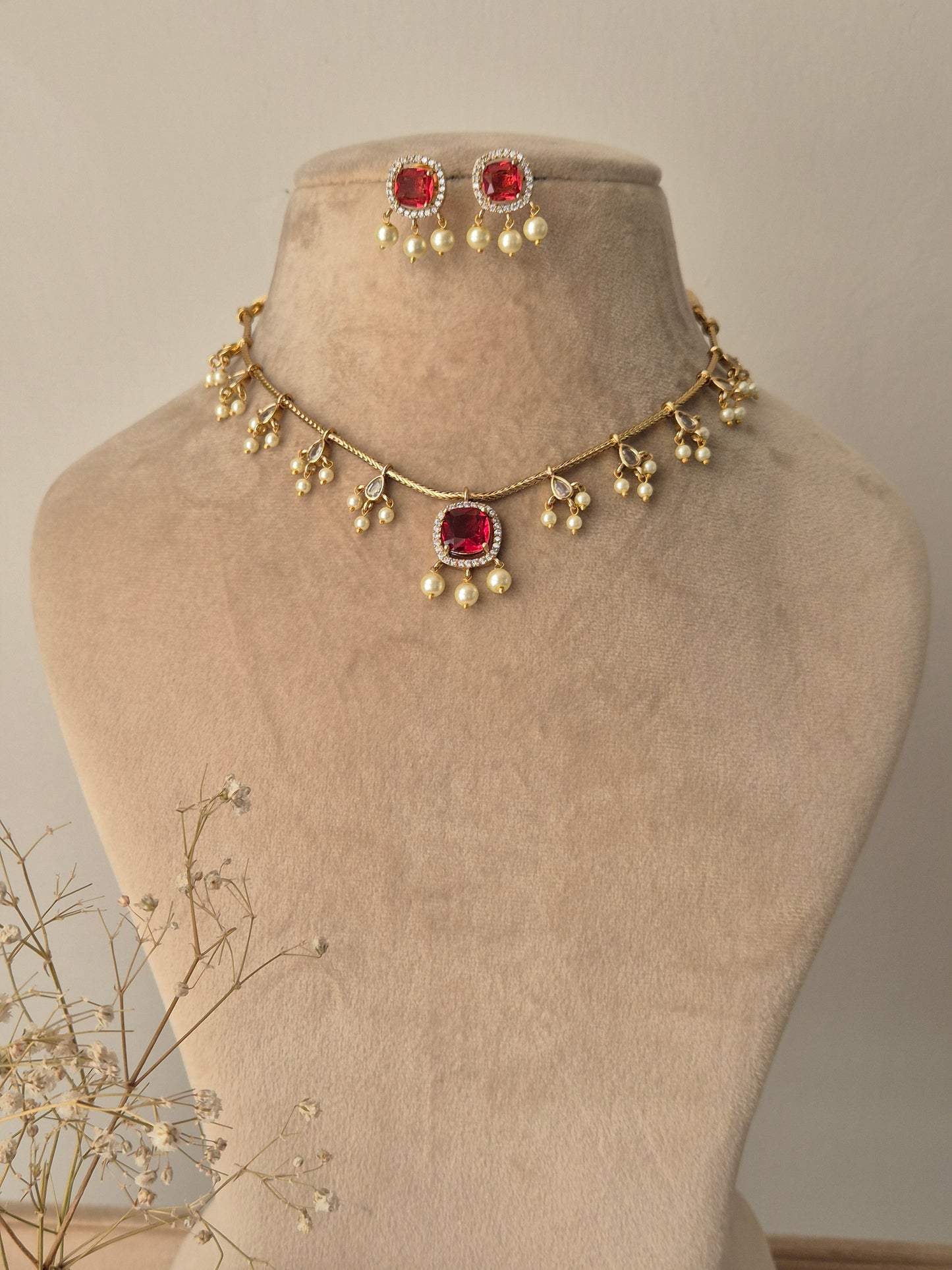 Gold-plated Garvita necklace set featuring ruby red square-cut gemstones, clear stone accents, and delicate pearl drops by naitri.in