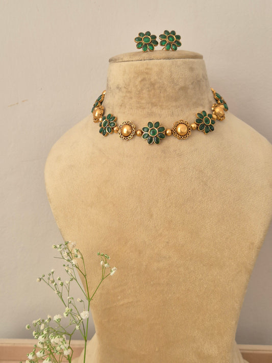 A gold-plated ethnic choker necklace featuring alternating textured round gold charms and green gemstone floral motifs,with matching flower stud earrings by naitri.in